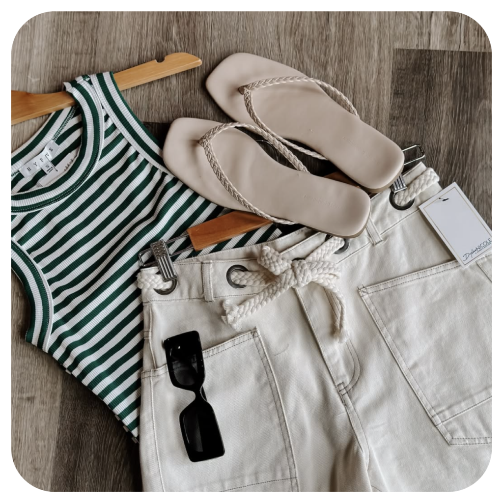 Striped green and white tank top with high-waisted cream shorts, rope belt, beige sandals, and black sunglasses on a wooden floor. Casual summer look.