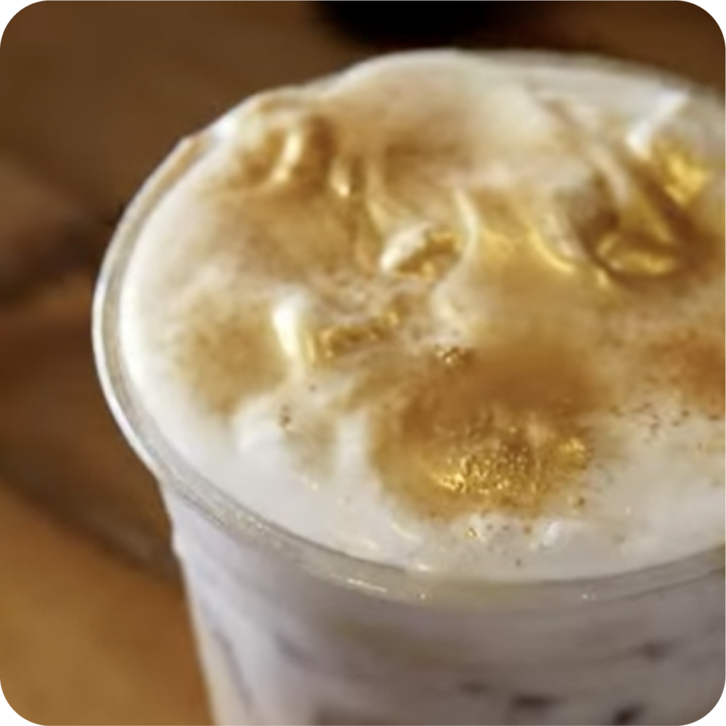 Close-up of a creamy iced coffee topped with fluffy foam and a sprinkle of golden glitter, creating a luxurious and indulgent look.